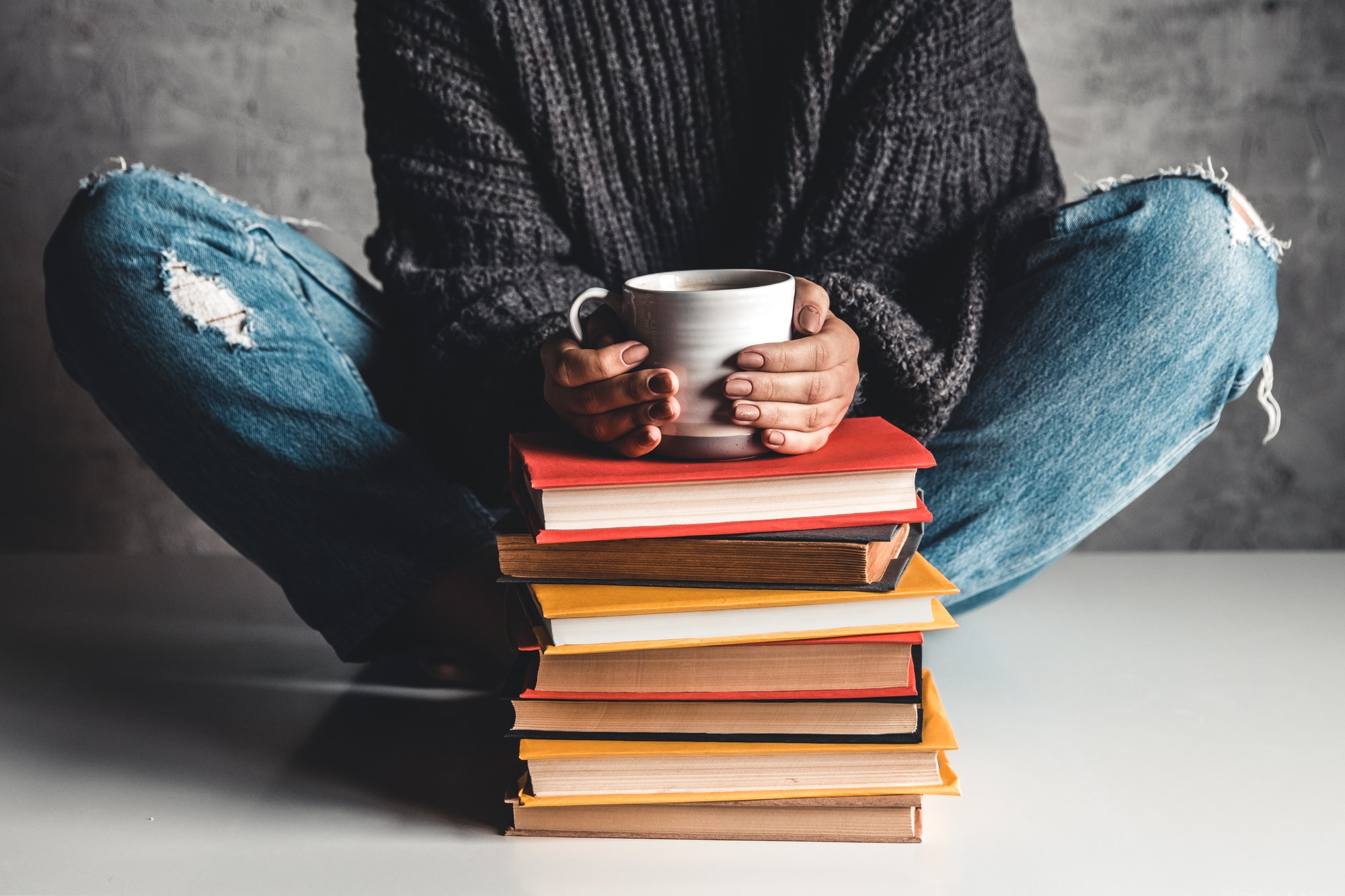 Stack of books with mug on top in front of woman reading book, education, training, hobbies